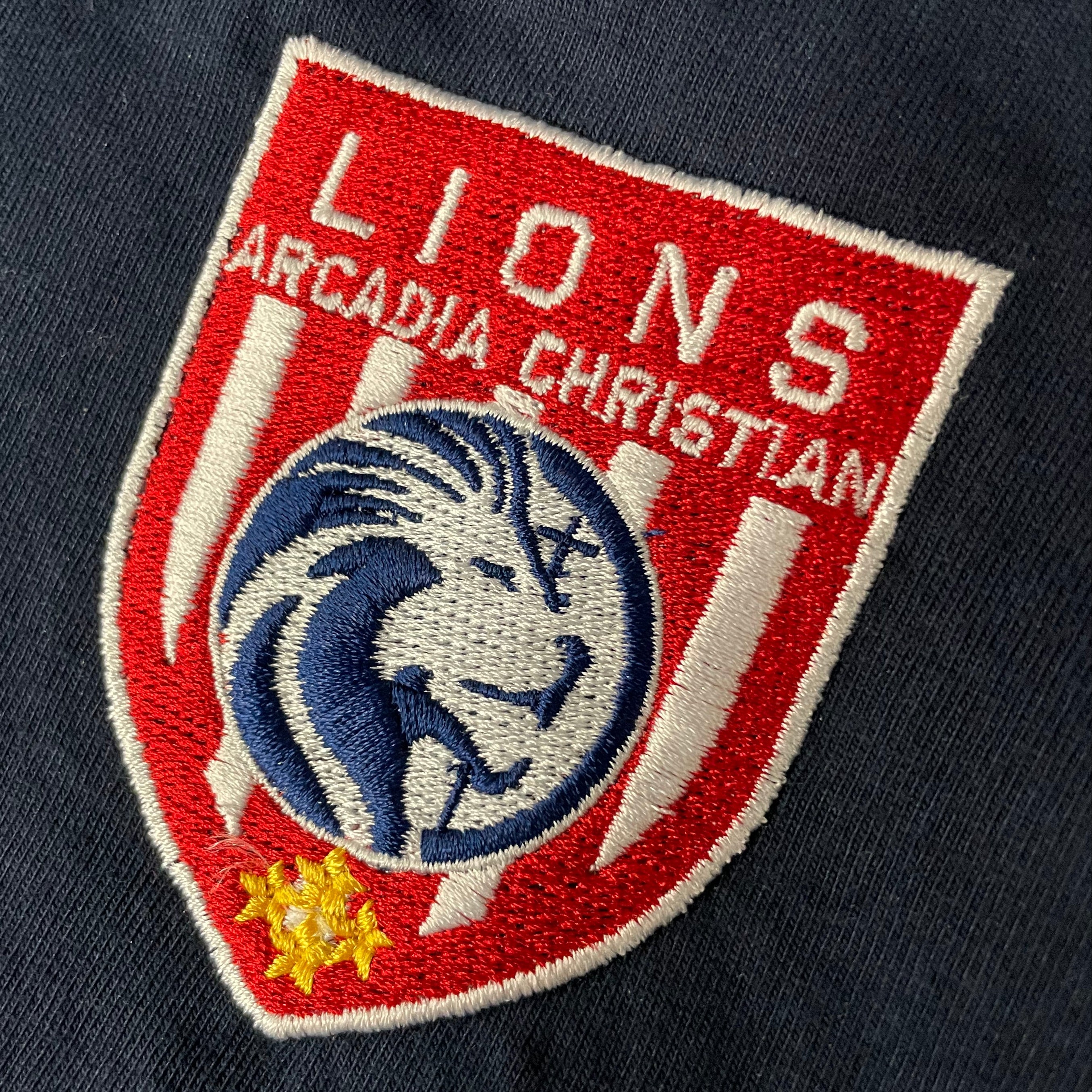 Embroidered patch on a dark fabric with 'Lions Arcadia Christian' text and lion design.