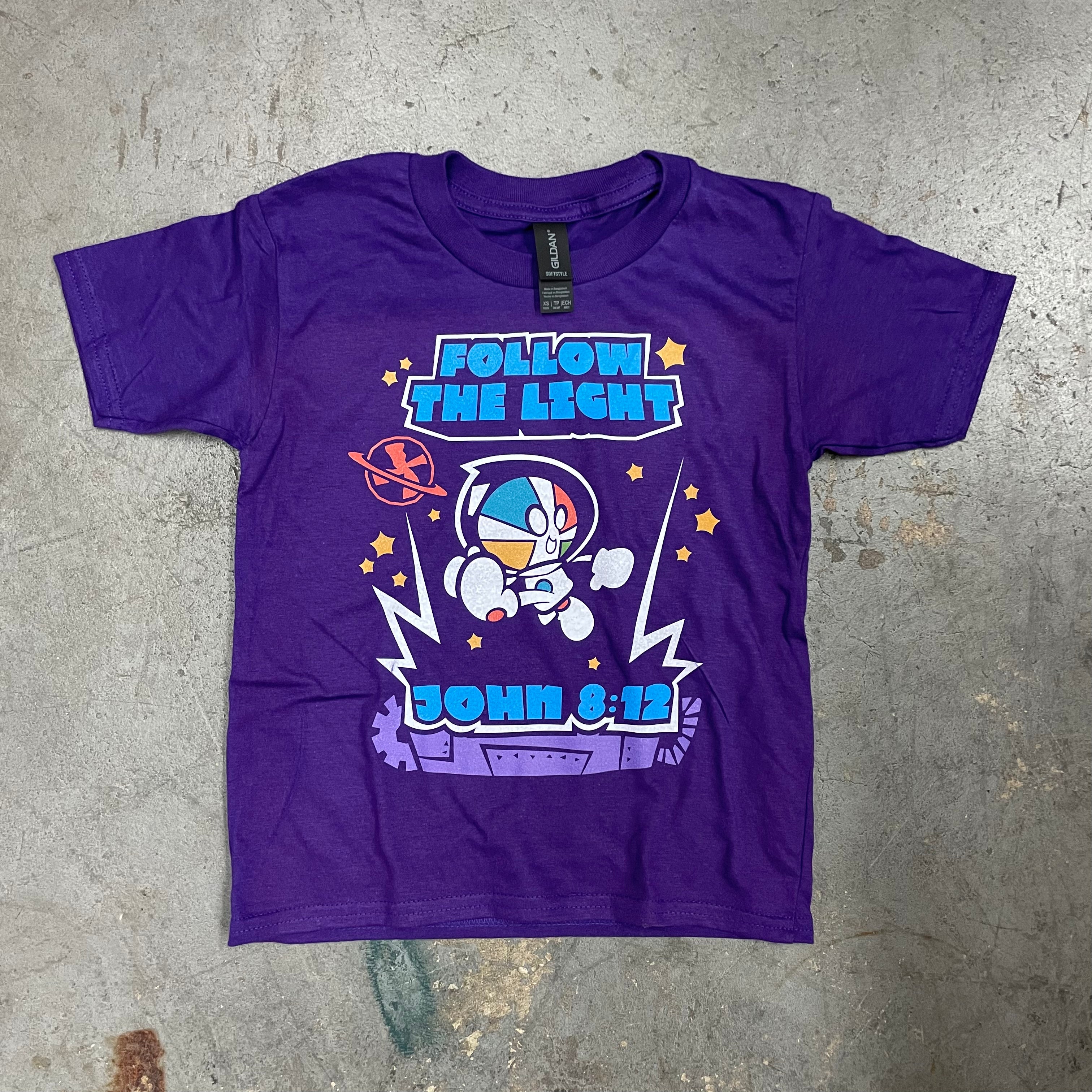 A purple short-sleeve t-shirt laid flat on a textured gray concrete surface. The shirt features a colorful graphic print of a cartoon astronaut with the text 'FOLLOW THE LIGHT' and 'JOHN 8:12'.